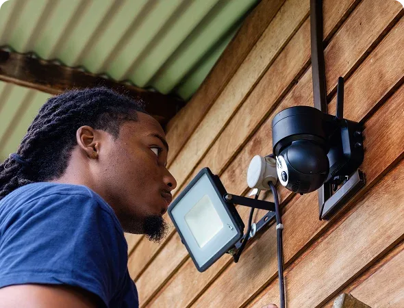 Technicien Kame Store installant une caméra et un projecteur sur une maison en bois en Guyane